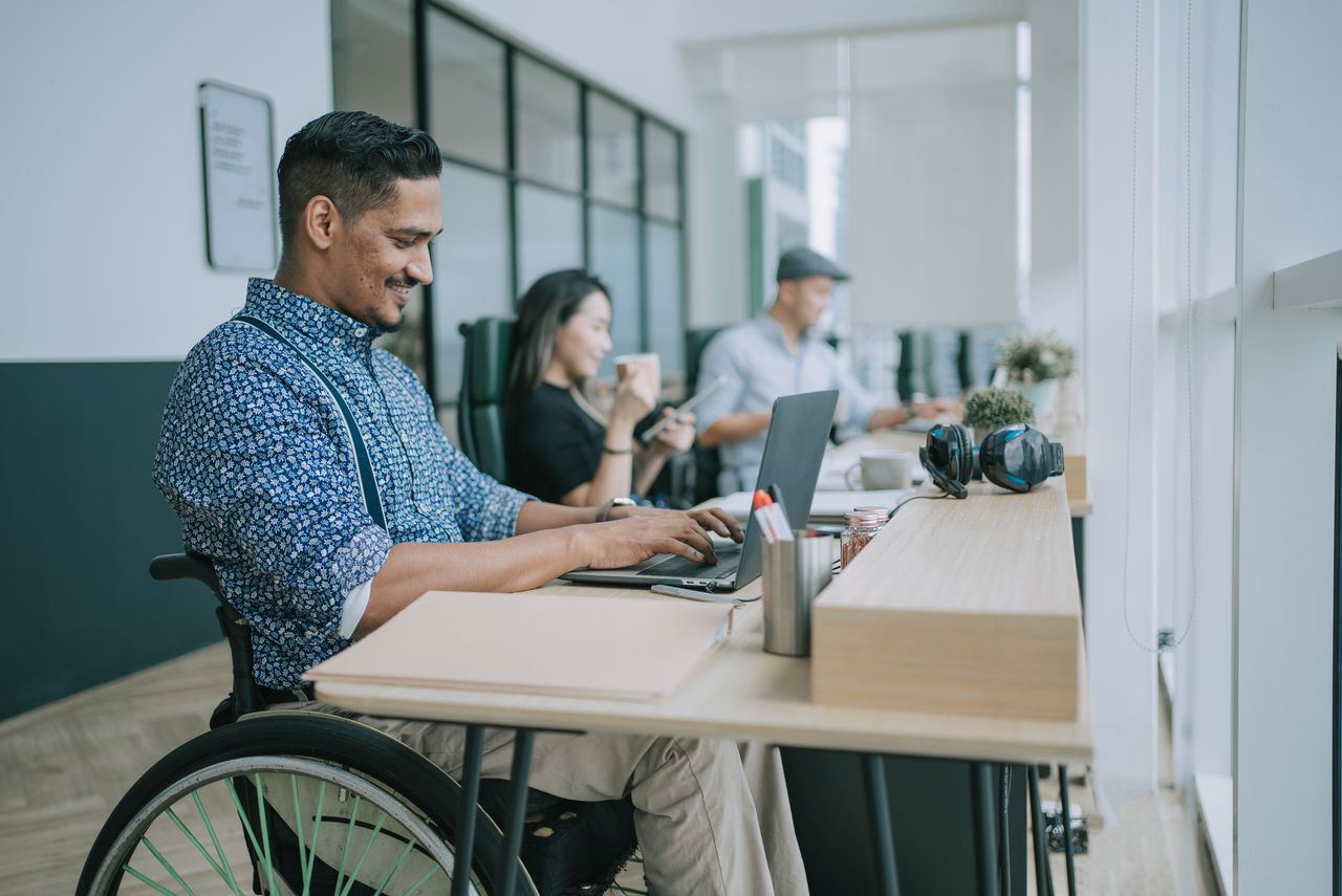 Man in wheelchair working on laptop in office smiling