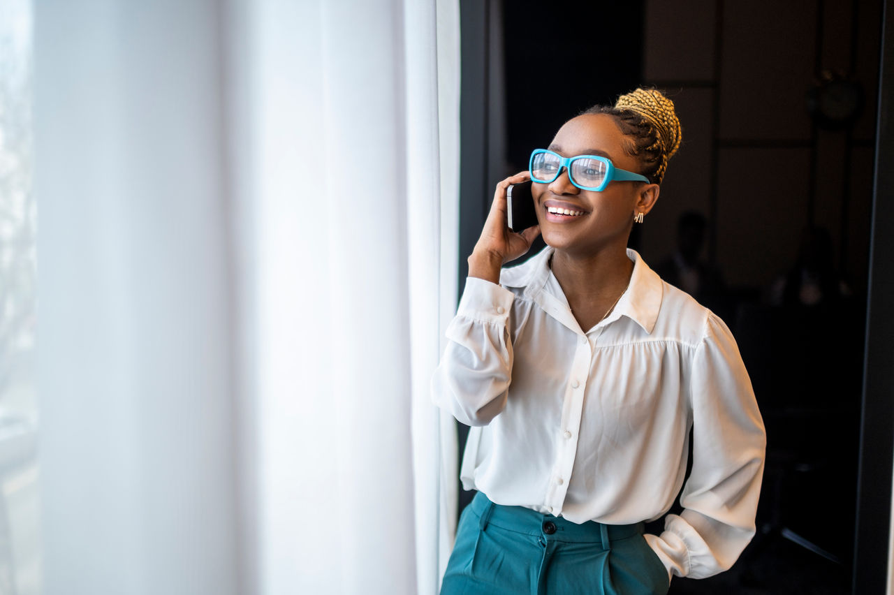 A woman with blue eyeglasses and a bun standing by the window