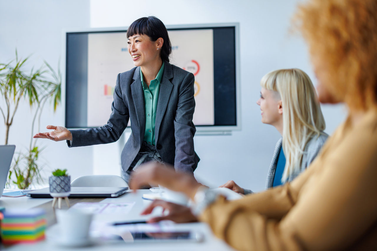 A person leading a business meeting with colleagues in a bright office setting, presenting data on a screen