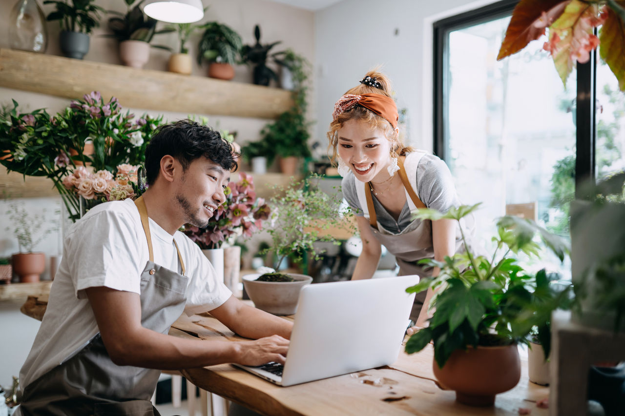 Small business owners in florist shop looking at laptop smiling