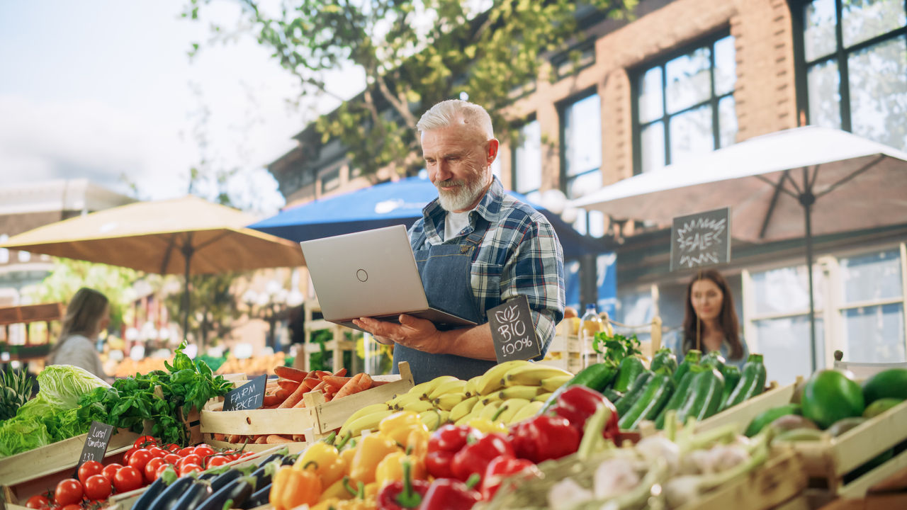Senior small business owner man checking laptop at his food stand in market