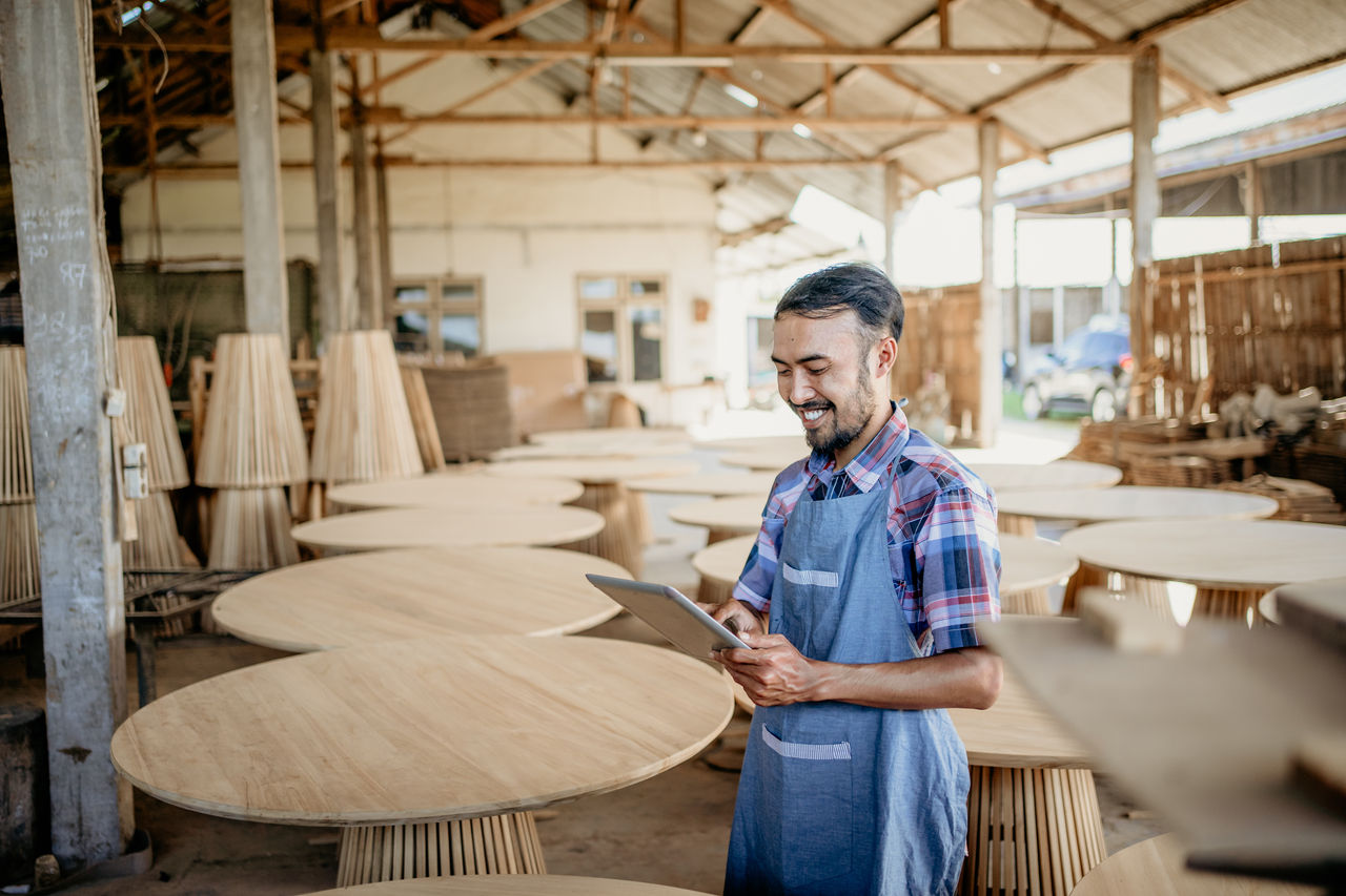 Small business owner using a tablet computer standing with wood craft shop in the background